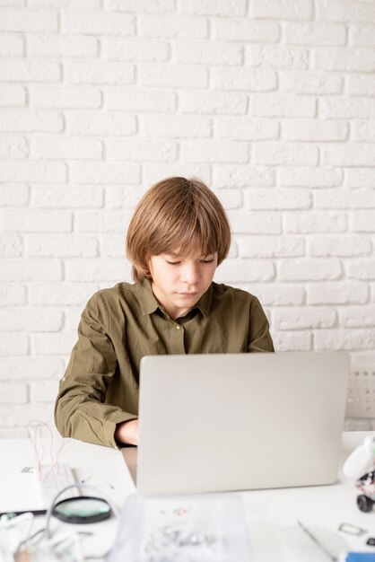 Jeune garçon en chemise verte travaillant ou étudiant sur l'ordinateur portable à la maison