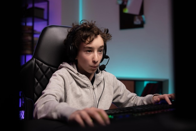 Un jeune garçon concentré aux cheveux bouclés passe du temps à l'ordinateur à jouer à des jeux vidéo multijoueurs avec l'équipe