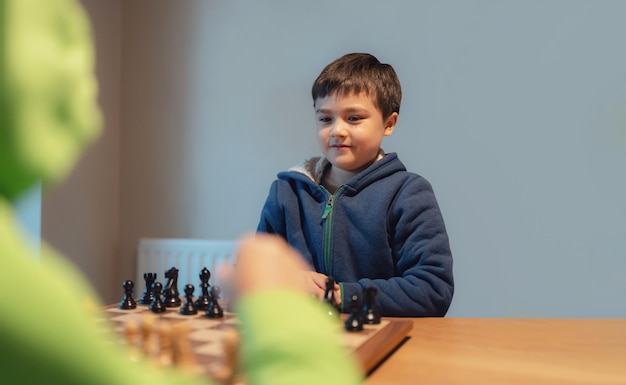 Jeune garçon concentré développant une stratégie d'échecs jouant à un jeu de société avec un ami ou une famille à la maison Activité ou passe-temps pour le concept familial