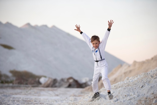 Un jeune garçon en costume d'astronaute américain saute sur fond de montagnes blanches