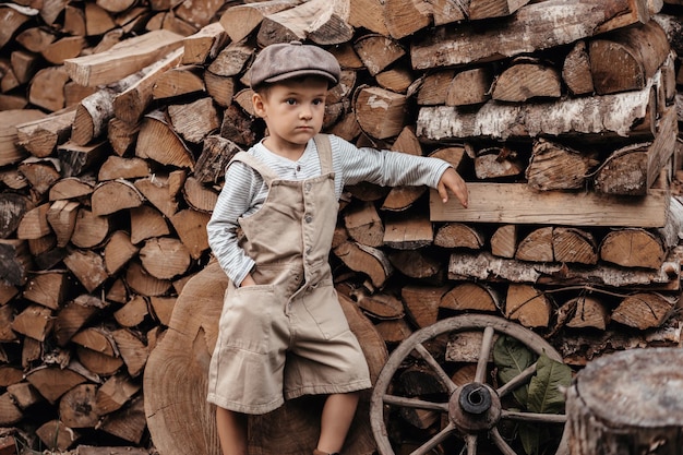 Un jeune garçon dans une casquette à côté d'un tas de bois dans un paysage naturel Libre donne à l'image une ambiance authentique Vintage Rustic