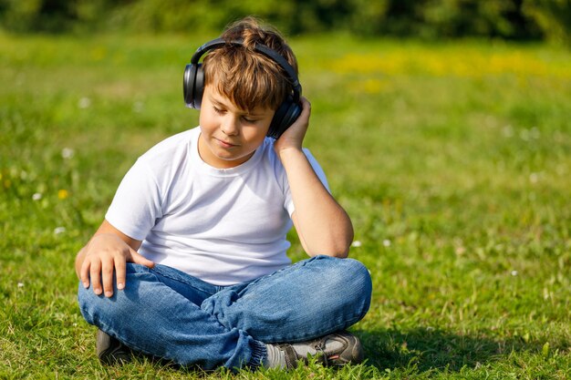 Jeune garçon avec des écouteurs écoutant de la musique alors qu'il était assis sur l'herbe dans le parc