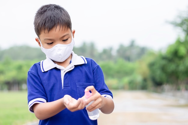 Jeune Garçon Enfant Asiatique Portant Un Masque En Tissu Et Tenant Un Vaporisateur D'alcool à La Main Pour Prévenir Le Coronavirus Ou La Maladie De Covid-19.