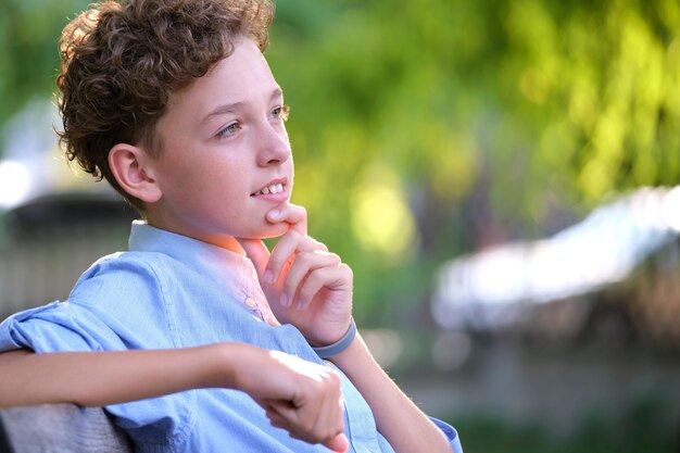 Jeune garçon enfant heureux se détendre assis sur un banc dans le parc d'été. Enfant positif profitant de l'été à l'extérieur. Concept de bien-être de l'enfant.