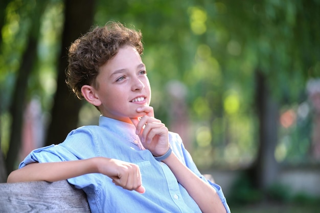 Jeune garçon enfant heureux se détendre assis sur un banc dans le parc d'été Enfant positif profitant de l'été à l'extérieur Concept de bien-être de l'enfant