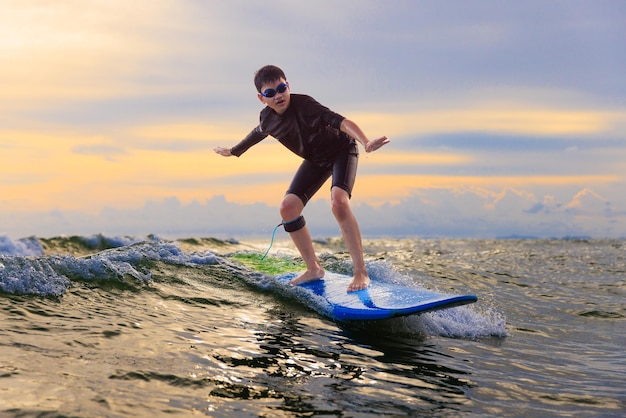 Photo jeune garçon enfant surfeur chevauchant des vagues avec une planche souple à rayong beach thaïlande rookie étudiant de planche de surf jouant sur l'eau dans un visage excité et une action amusante