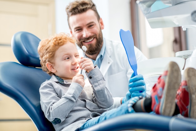 Jeune garçon excité regardant le miroir dentaire assis sur la chaise avec le dentiste au cabinet dentaire