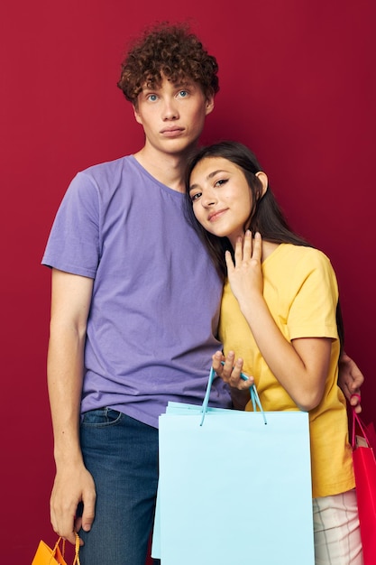 Jeune garçon et fille en T-shirts colorés avec des sacs Shopping fond rouge inchangé