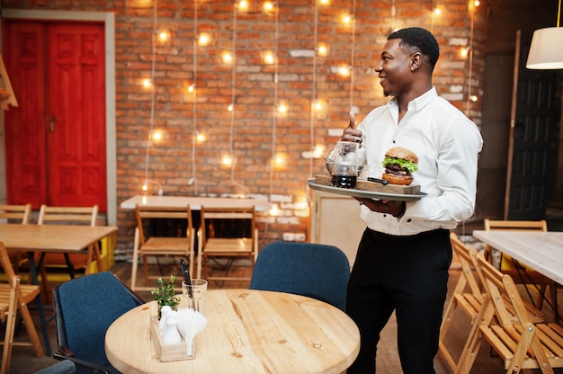 Jeune garçon homme tient un plateau avec burger au restaurant et montrer le pouce vers le haut