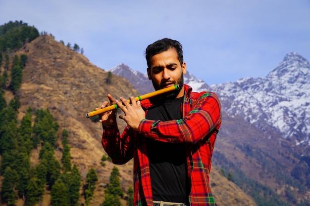 Jeune garçon jouant de la flûte indienne bansuri dans les montagnes