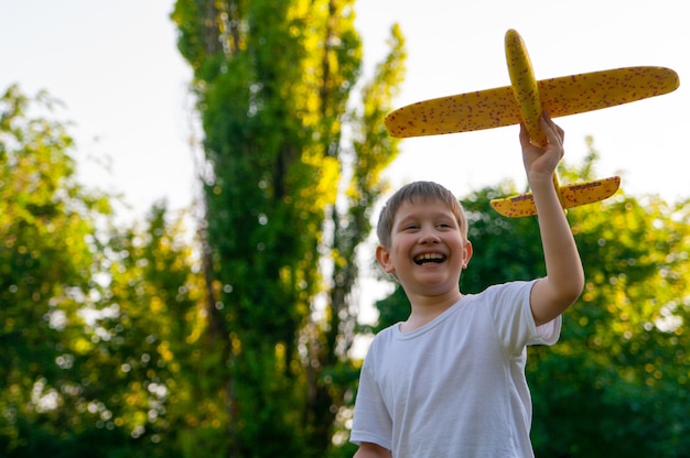 Jeune garçon jouant avec un planeur jouet dans le parc le jour d'été au coucher du soleil.