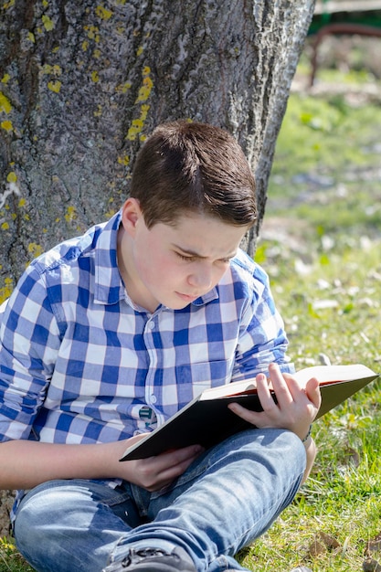 Jeune garçon lisant un livre dans les bois avec une faible profondeur de champ et un espace de copie