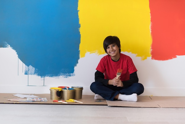 jeune garçon peintre se reposant après avoir peint le mur, assis sur le sol dans une nouvelle maison