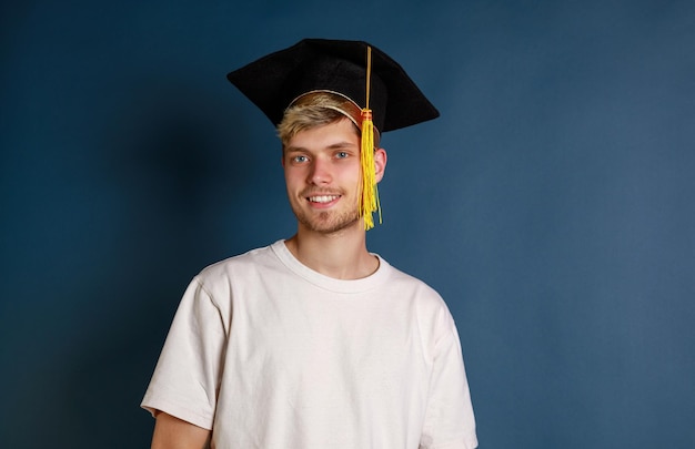 Jeune garçon portant une casquette de graduation et sranding sur fond bleu