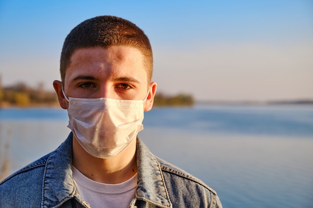 Jeune garçon portant un masque protecteur chirurgical pour prévenir les coronavirus sur le fond du lac.