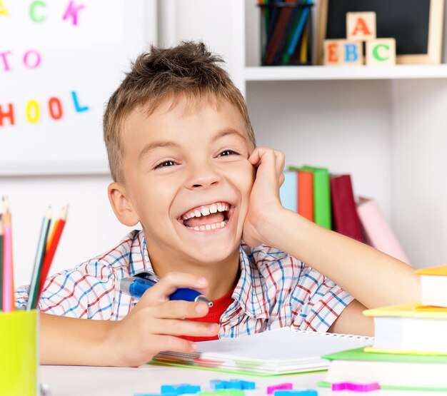 Un jeune garçon souriant fait ses devoirs à la table.