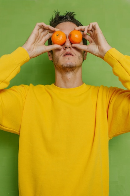 Jeune garçon tenant deux oranges dans ses yeux sur fond vert, photo verticale