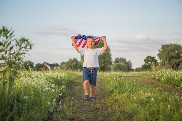Jeune garçon tenant un drapeau américain au coucher du soleil dans le champ