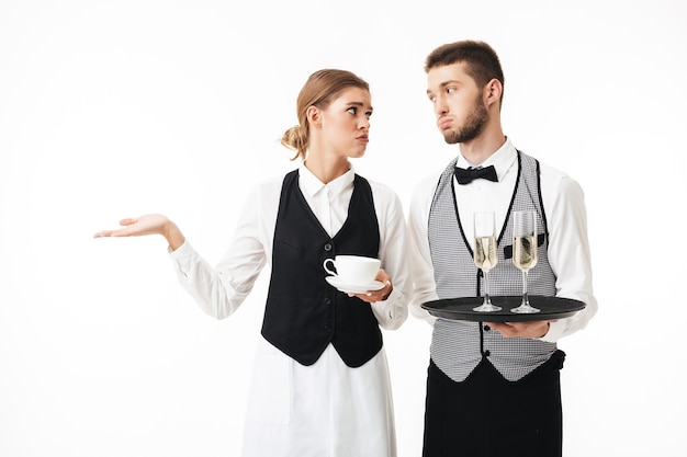 Jeune garçon tenant un plateau avec des verres de champagne et une serveuse triste tenant une tasse de café dans les mains tout en lassant