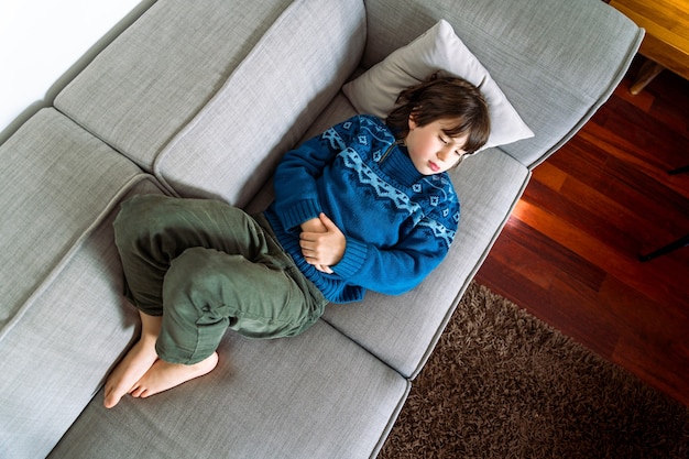 Jeune garçon triste s'endormant sur le canapé à la maison. L'enfant malade ne se sent pas bien.