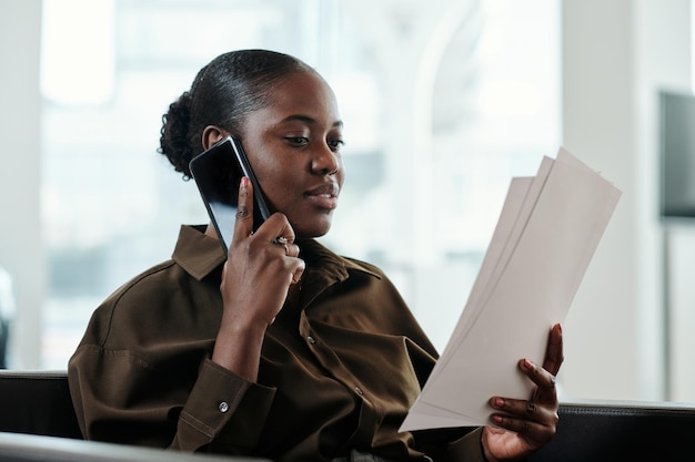 Jeune gestionnaire confiant en vêtements décontractés intelligents lisant des journaux et parlant au téléphone