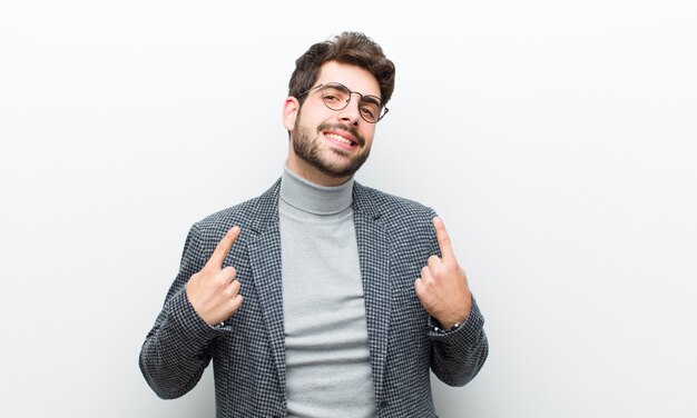 Jeune gestionnaire homme avec une mauvaise attitude à la recherche de fierté et d'agressivité, pointant vers le haut ou faisant signe avec les mains contre le mur blanc