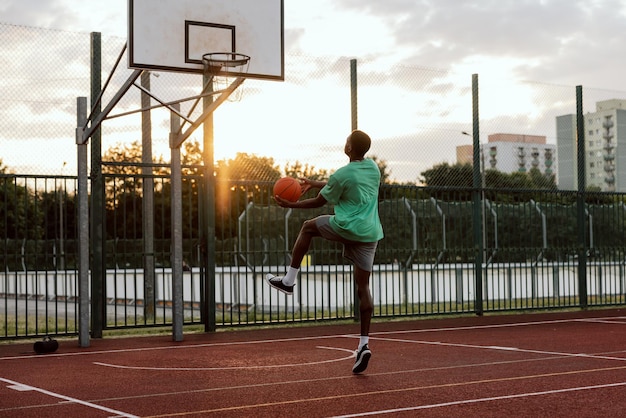 Jeune grand garçon afro-américain essayant de faire du slam dunk montrant des compétences en jouant à l'extérieur