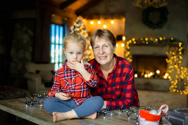 Photo une jeune grand-mère avec sa petite petite-fille qui est assise sur une table et mange des bonbons provenant d'un cadeau de noël. notion de famille matin de noël.