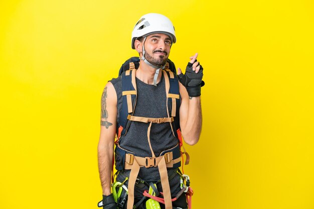 Jeune grimpeur caucasien isolé sur fond jaune avec les doigts croisés et souhaitant le meilleur