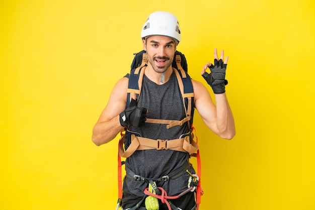 Jeune grimpeur caucasien isolé sur fond jaune montrant le signe ok et le geste du pouce vers le haut