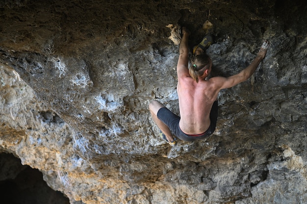 Jeune grimpeur mâle bouldering une paroi rocheuse dans une grotte