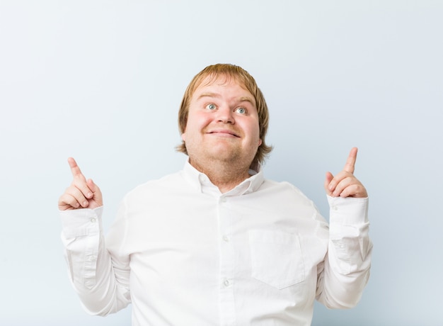 Un jeune gros homme rousse authentique indique avec les deux doigts avant en haut montrant un espace vide.