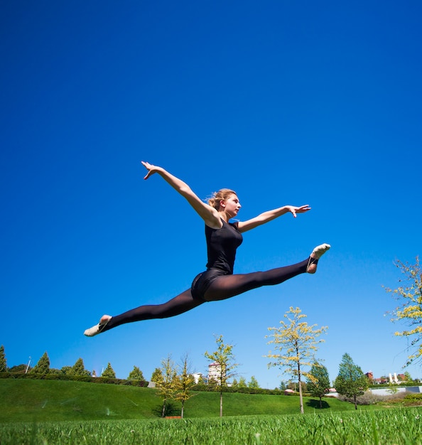 Jeune gymnaste souriante saute en deux et flotte au-dessus de la terre.