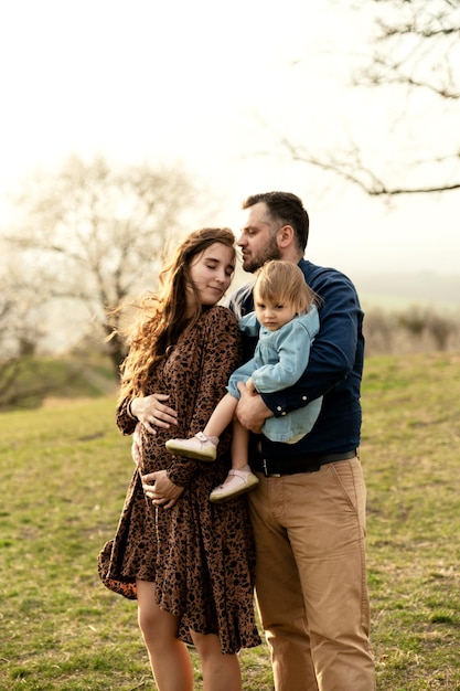 Une jeune et heureuse famille se promène dans la nature avec leur fille enceinte en promenade avec sa famille promenade printanière