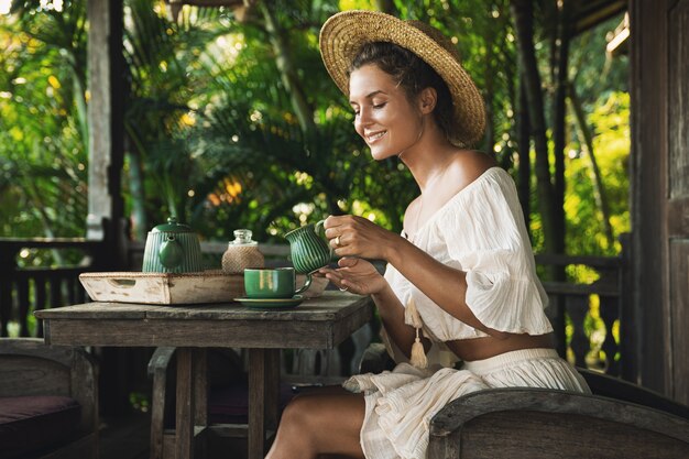 Jeune et heureuse femme assise sur la terrasse d'été et boire du café