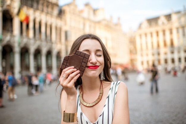 Jeune et heureuse femme avec une barre de chocolat noir debout à l'extérieur sur la Grand Place à Bruxelles en Belgique. La Belgique est célèbre pour son chocolat