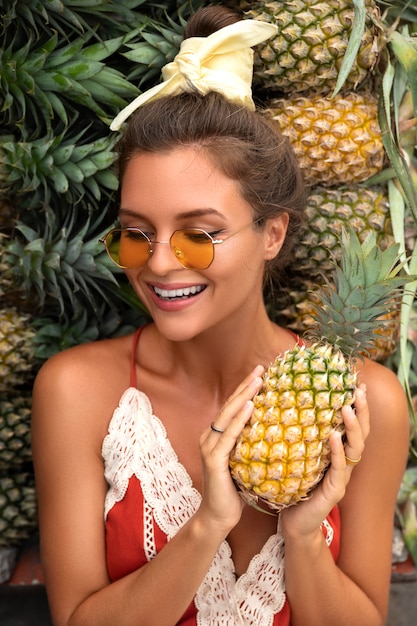 Jeune et heureuse femme avec un tas d'ananas au marché