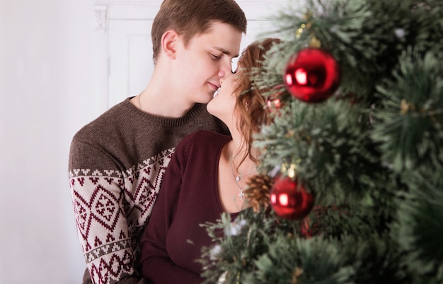 Jeune, heureux, couple, embrasser, près, arbre noël, célébrer, nouvel an, ensemble, sourire