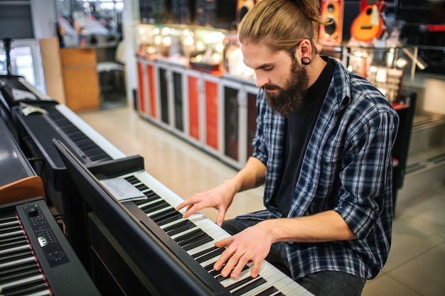 Jeune hipster concentré s'asseoir et jouer sur le clavier. Il le regarde. Guy est seul dans la chambre.