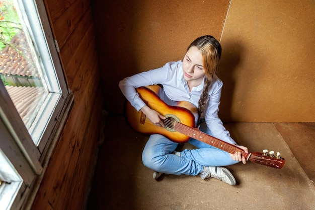 Jeune hipster femme assise sur le sol et jouant de la guitare à la maison Adolescente apprenant à jouer de la chanson et à écrire de la musique dans sa chambre Mode de vie passe-temps se détendre Concept d'éducation aux loisirs instrument