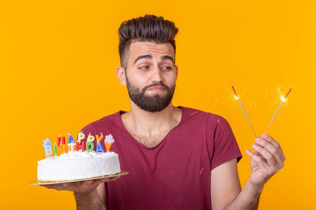 Jeune hipster masculin avec une barbe tenant un gâteau avec l'inscription joyeux anniversaire félicitations pour l'anniversaire et les vacances. Concept de promotions et de remises.