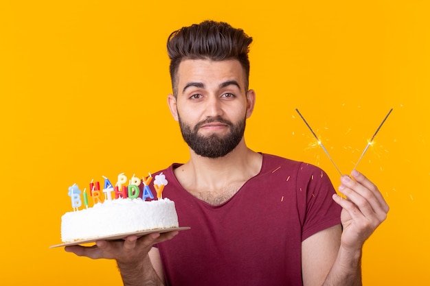 Jeune hipster masculin avec une barbe tenant un gâteau avec l'inscription joyeux anniversaire félicitations pour l'anniversaire et les vacances. Concept de promotions et de remises.