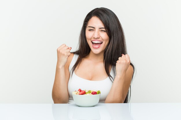 Jeune, hispanique, femme, manger, fruit, bol, applaudissement, insouciant, excité