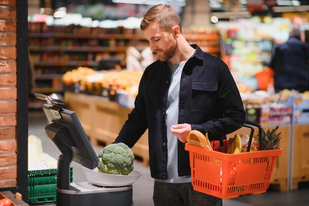 Jeune homme acheter des produits d'épicerie au supermarché Autres clients en arrière-plan Concept de consommation