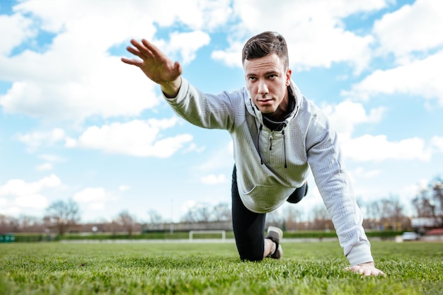 Jeune homme actif qui s'étire et fait des exercices dans l'espace public sur un stade vide.