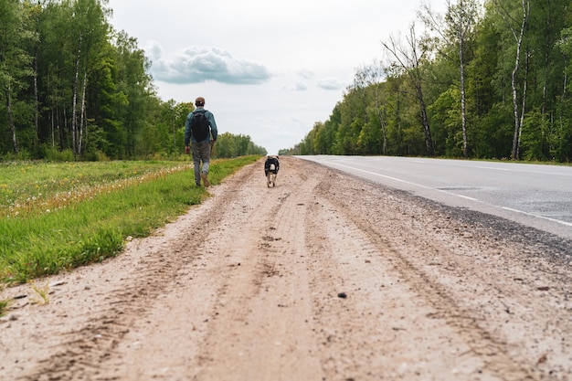 Jeune homme, un adolescent avec un chien marche sur le bord de la route