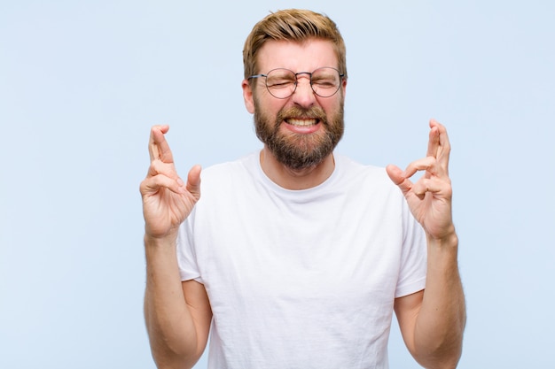 Jeune Homme Adulte Blond Souriant Et Traversant Avec Anxiété Les Deux Doigts, Inquiet Et Souhaitant Ou Souhaitant Bonne Chance