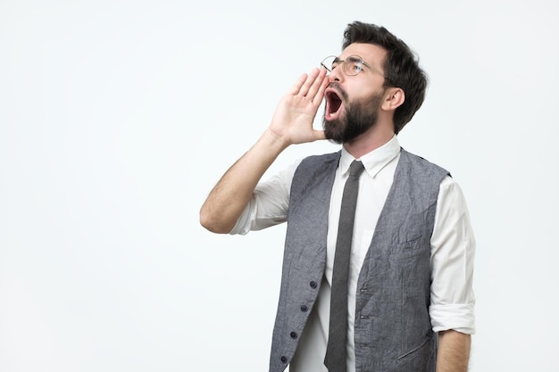 Jeune homme adulte hispanique avec barbe criant et criant fort à côté avec la main sur la bouche