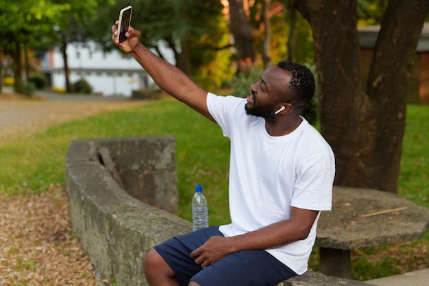 Jeune homme adulte se reposant dans le parc après avoir fait du jogging et pris un mode de vie sain selfie