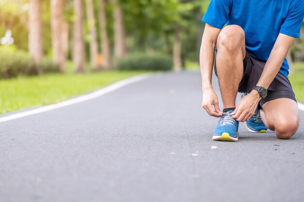 Jeune homme adulte en tenue de sport attachant les lacets dans le parc en plein air, homme coureur athlète prêt pour la course et le jogging le matin. Exercice, bien-être, mode de vie sain et concept d'entraînement